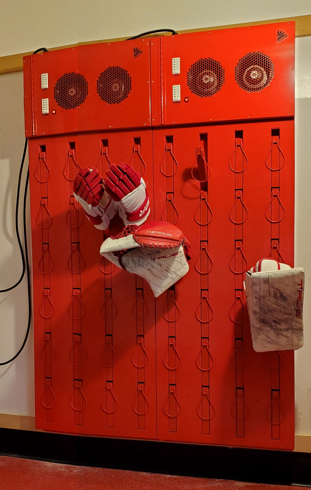 Hockey glove dryer. 12 pair wall mounted. Space saving wall mounted design. Stainless steel and aluminum construction. Sleek thin with retracting pegs. Loops for gloves. High flow for fast drying and slow drying option.  Painted  red for Boston University